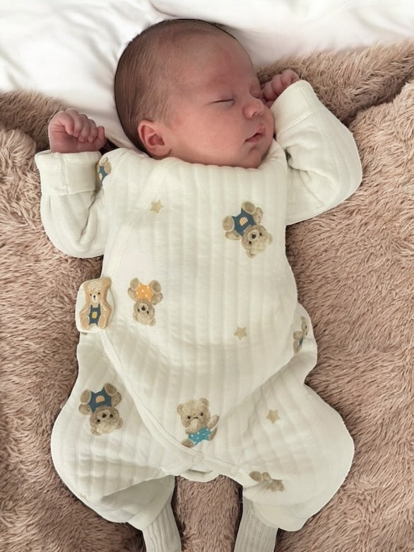 Newborn baby lying on a soft neutral blanket while wearing the cream teddy and star romper