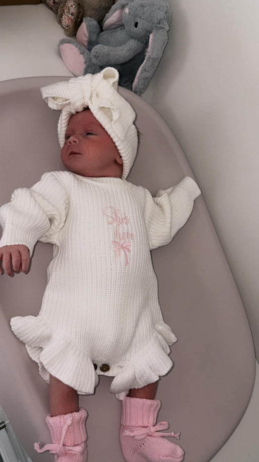 Baby girl announcement romper with she’s here embroidered lettering and cute bow detail 
