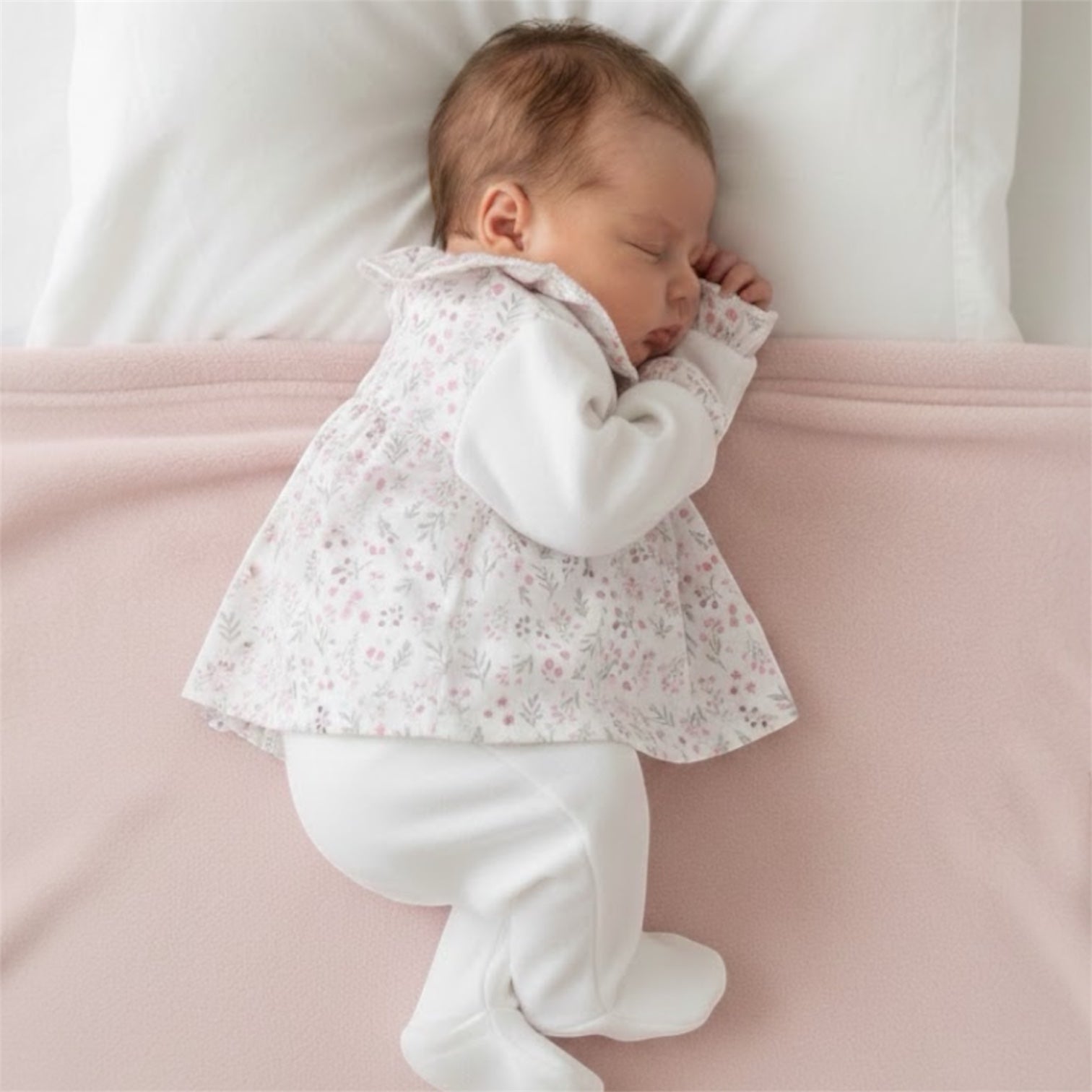 Baby sleeping on their side in a delicate floral baby sleepsuit, photographed on a neutral pink background
