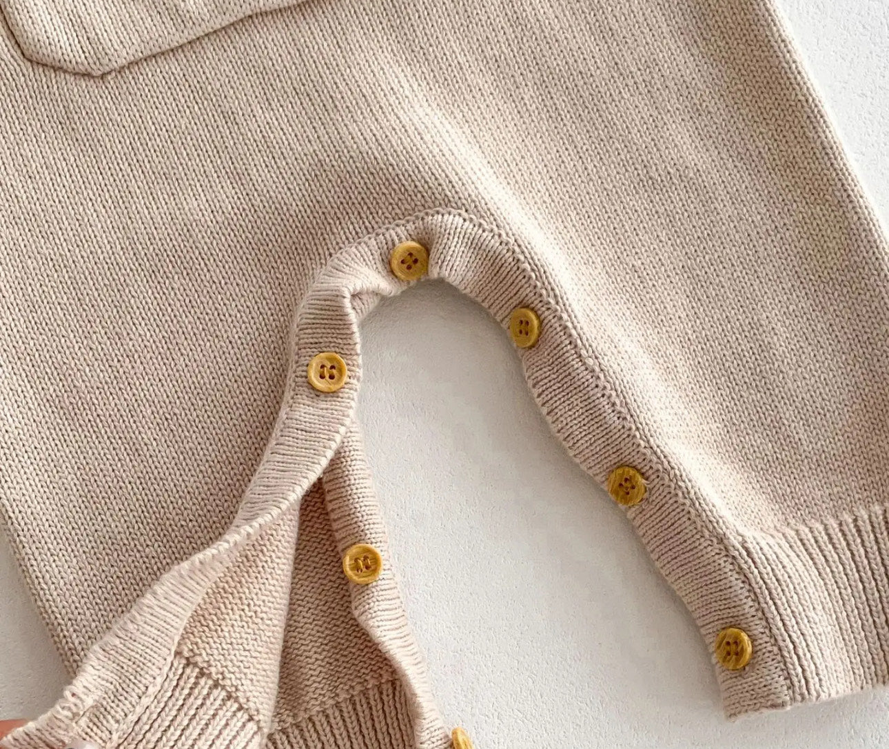 Close-up of the button closures and soft knit fabric on the beige Cosi Bear Pocket Onesie