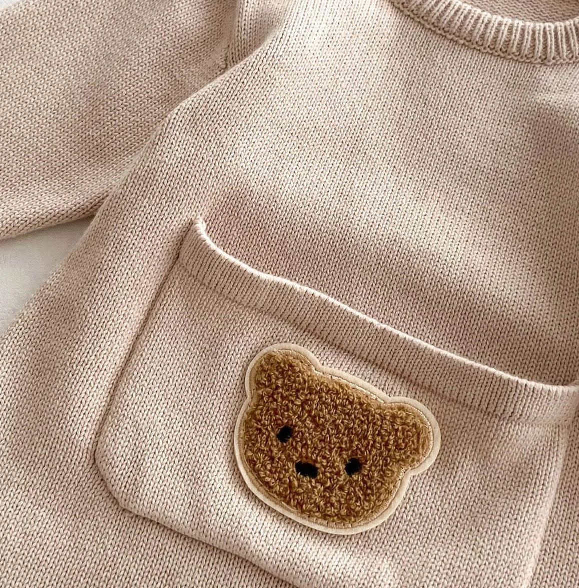 Close-up of the teddy bear pocket detail on the beige Cosi Bear Pocket Onesie