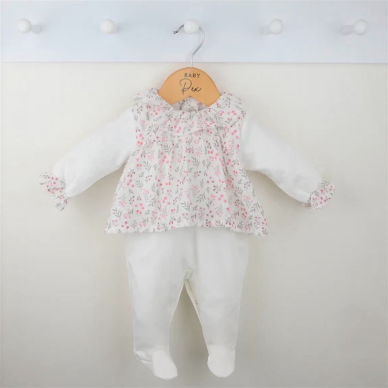 Floral baby sleepsuit displayed on a wooden hanger, showing the full two-piece outfi