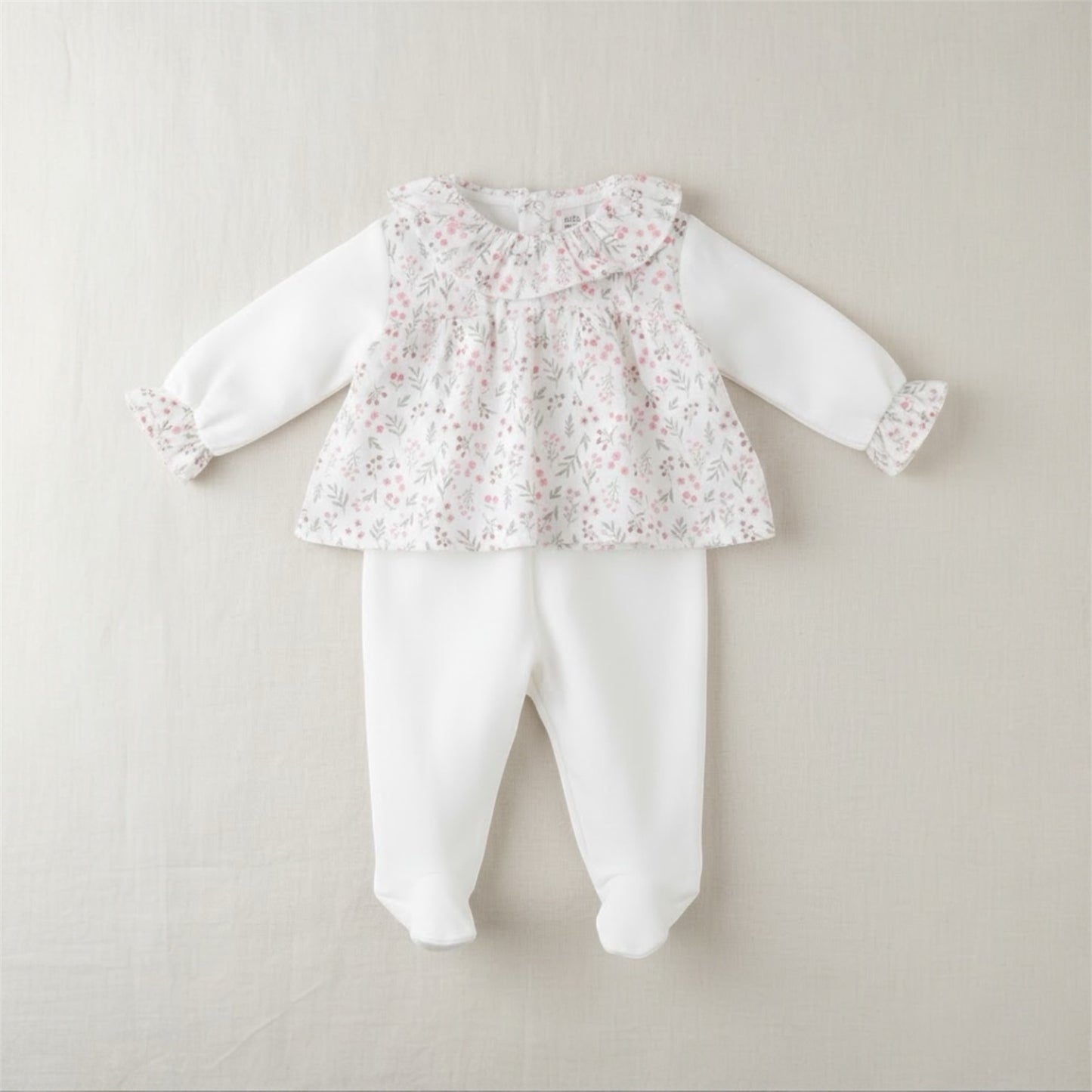 Flat lay of a floral baby sleepsuit set with matching trousers on a neutral background