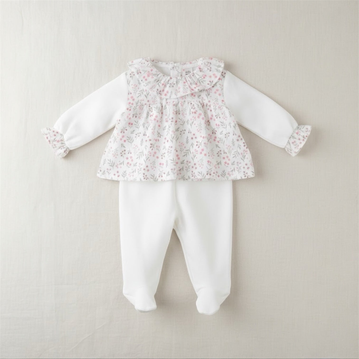 Flat lay of a floral baby sleepsuit set with matching trousers on a neutral background