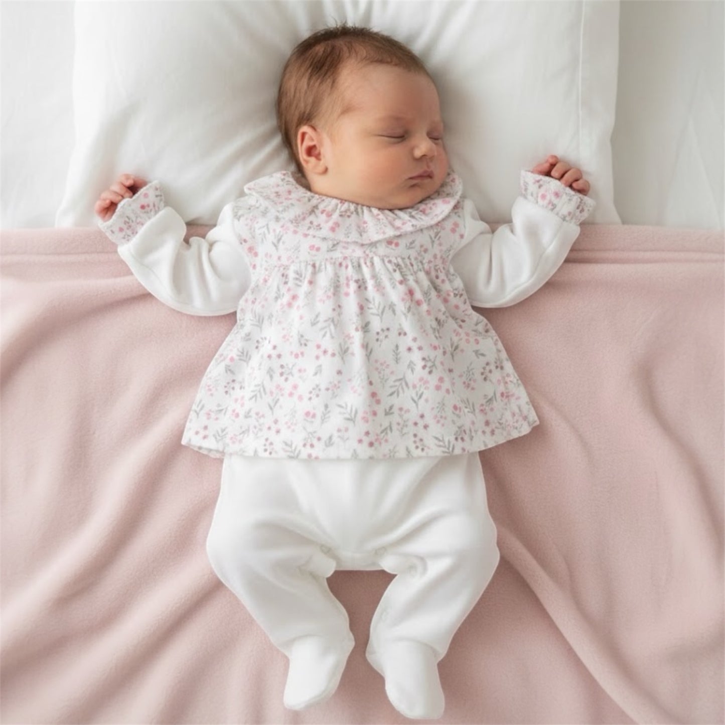 Newborn baby wearing a soft floral sleepsuit, lying on a pale pink blanket