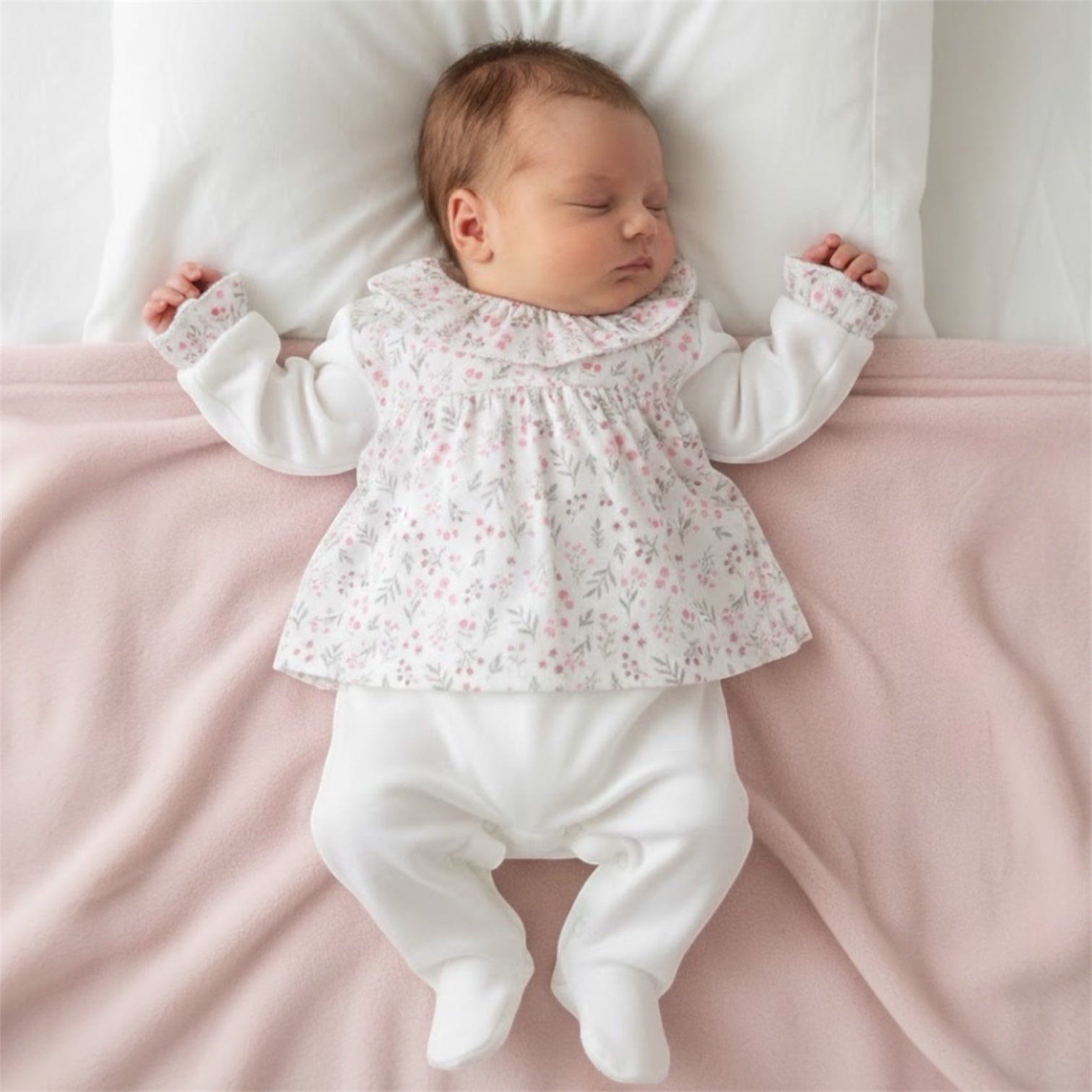 Newborn baby wearing a soft floral sleepsuit, lying on a pale pink blanket