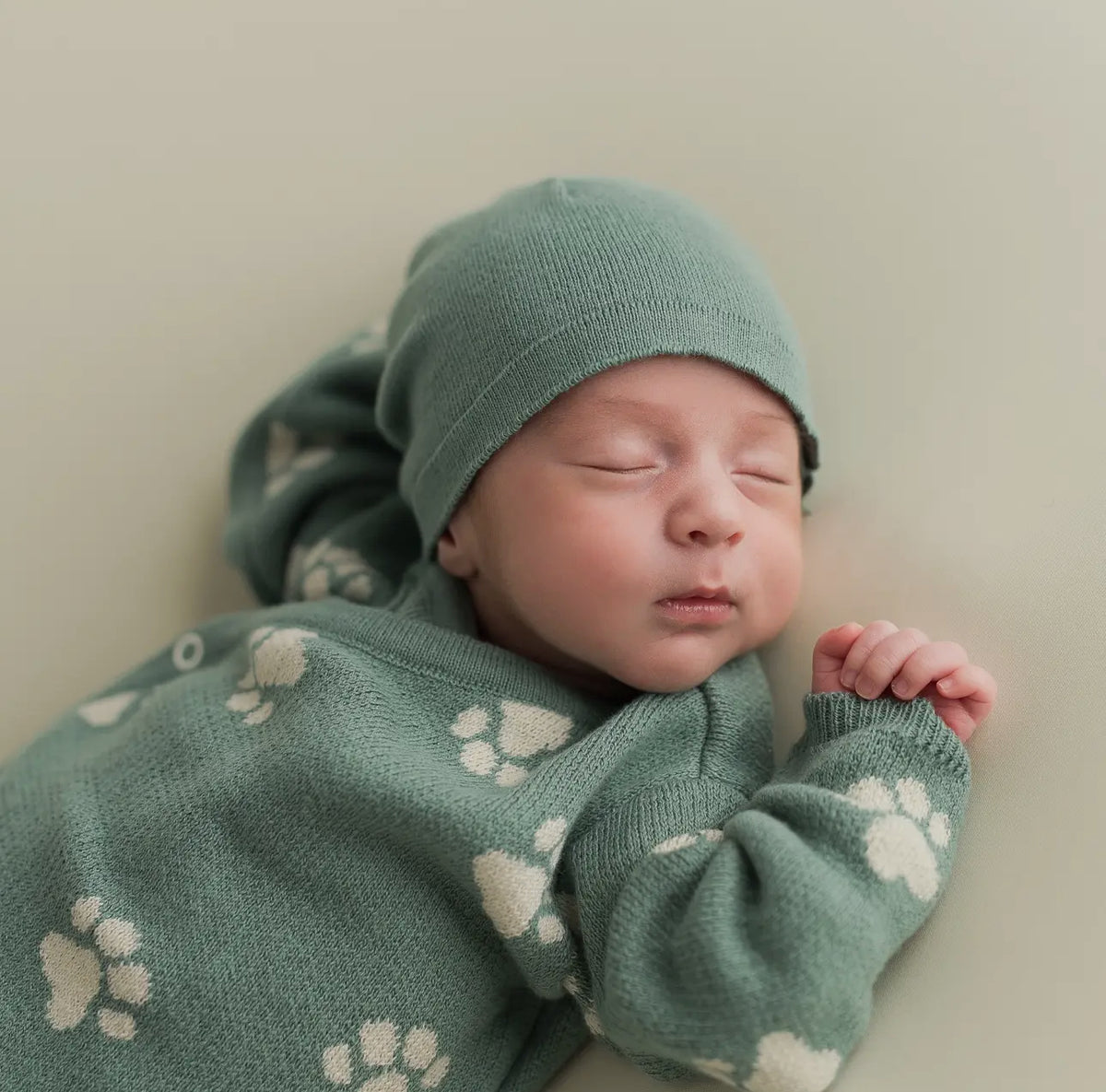 Close-up of a sleeping newborn baby wearing the Little Paws organic sage green beanie and matching paw-print sweater.