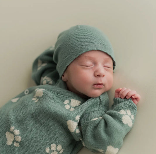 Close-up of a sleeping newborn baby wearing the Little Paws organic sage green beanie and matching paw-print sweater.