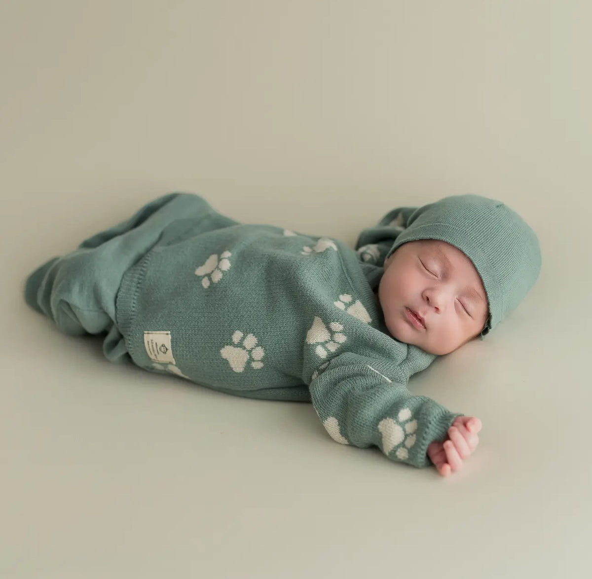Side view of a sleeping infant in the Little Paws 3-piece organic cotton set, showing the full sage green outfit with white paw-print pattern.