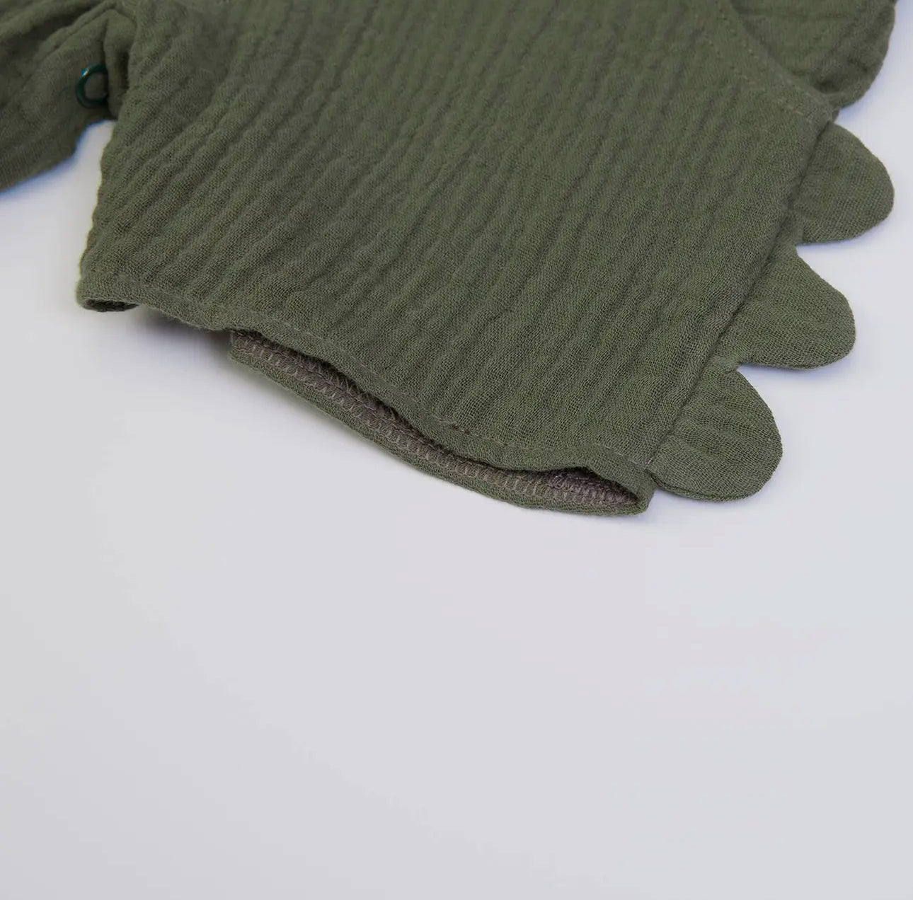 Close-up of the scalloped hem detail on olive green muslin baby dungarees, showing soft textured fabric