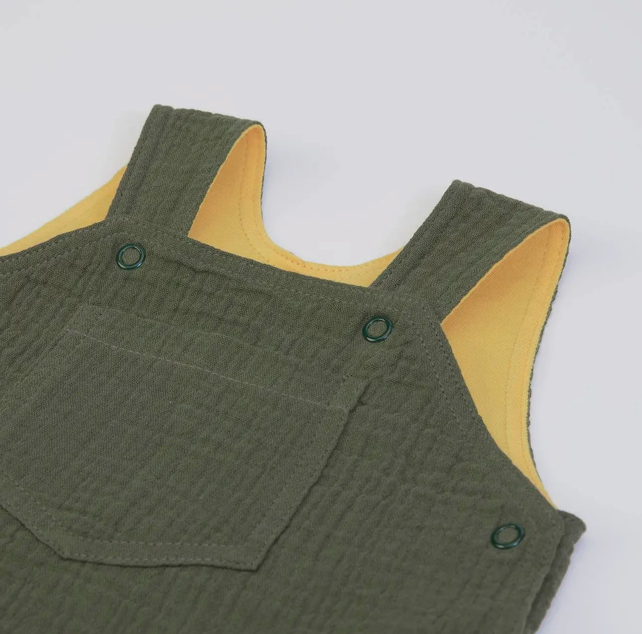 Close-up of the strap and button fastening on olive green muslin baby dungarees
