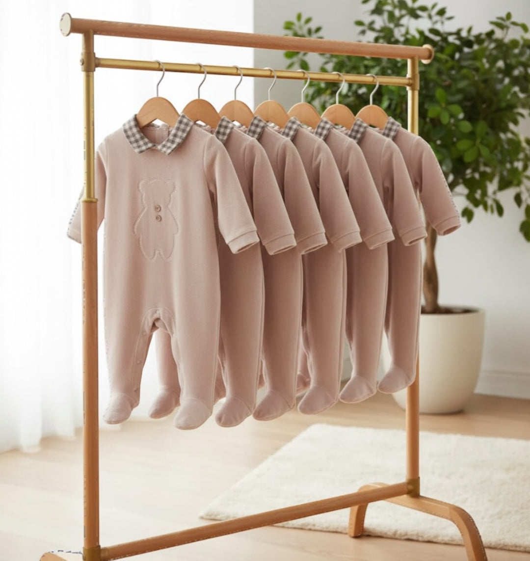 Soft velvet bear embroidered footed baby onesies displayed on a clothing rail, showing the full size range