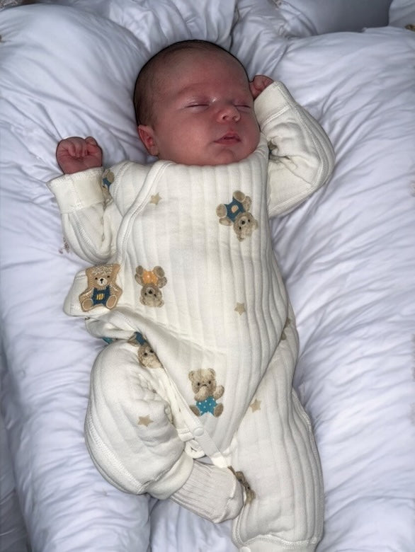 Newborn baby sleeping peacefully while wearing the cream teddy and star romper