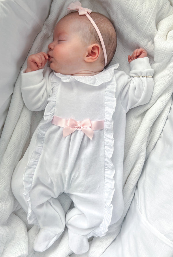 Newborn baby lying comfortably while wearing the white Victoria velour sleepsuit with delicate frill trim