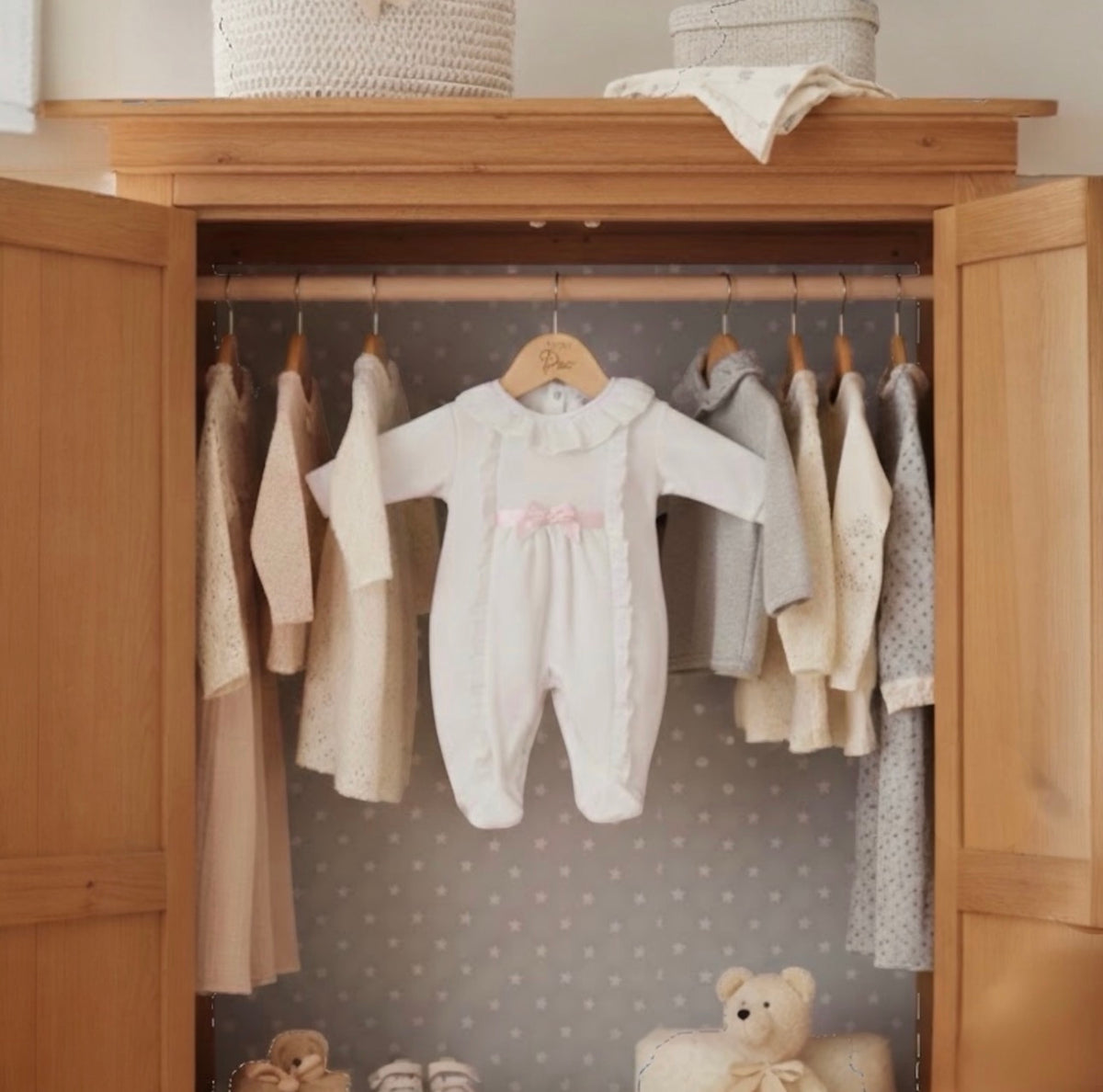 White Victoria velour baby sleepsuit displayed hanging in a nursery wardrobe alongside coordinating pieces